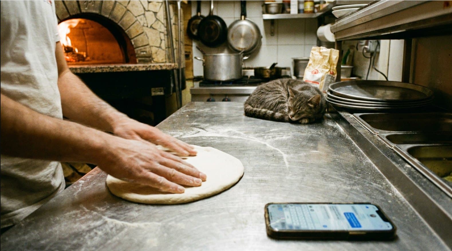 Pizzaiolo qui étale une pâte sur un comptoir fariné, four à bois allumé